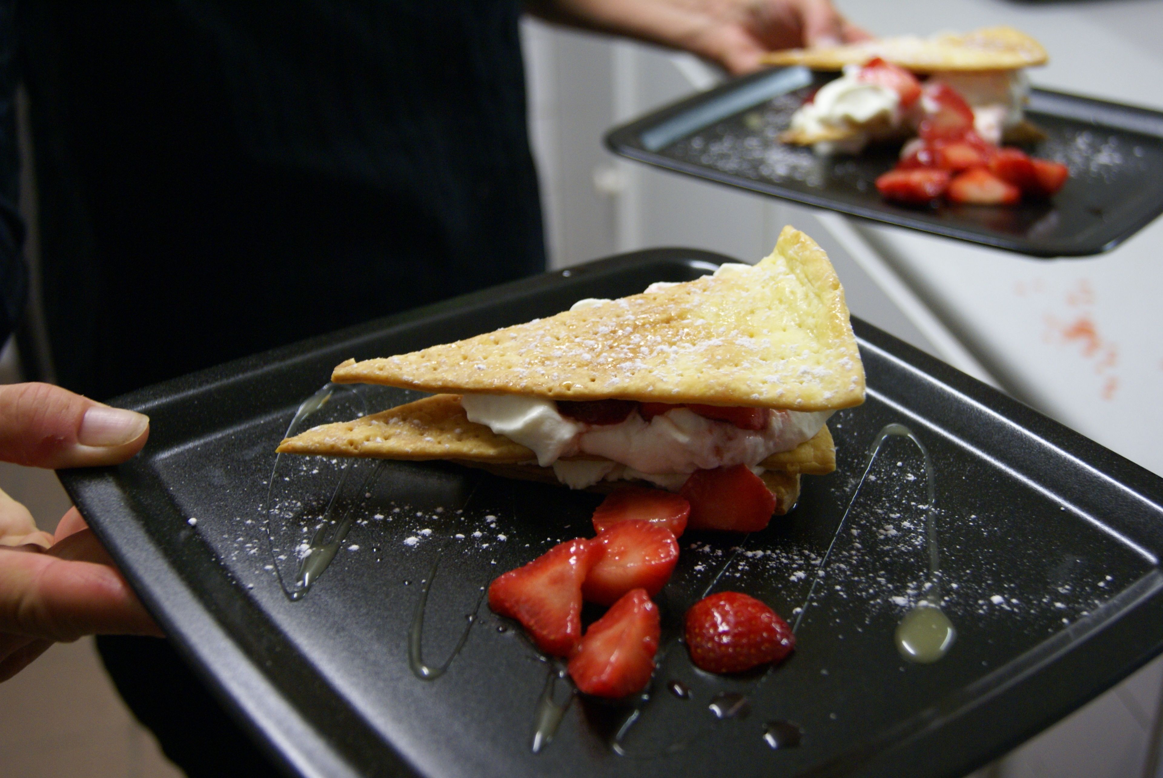 Een rijk gevulde dessertschaal met een driehoekig gebakje, slagroom en aardbeien.