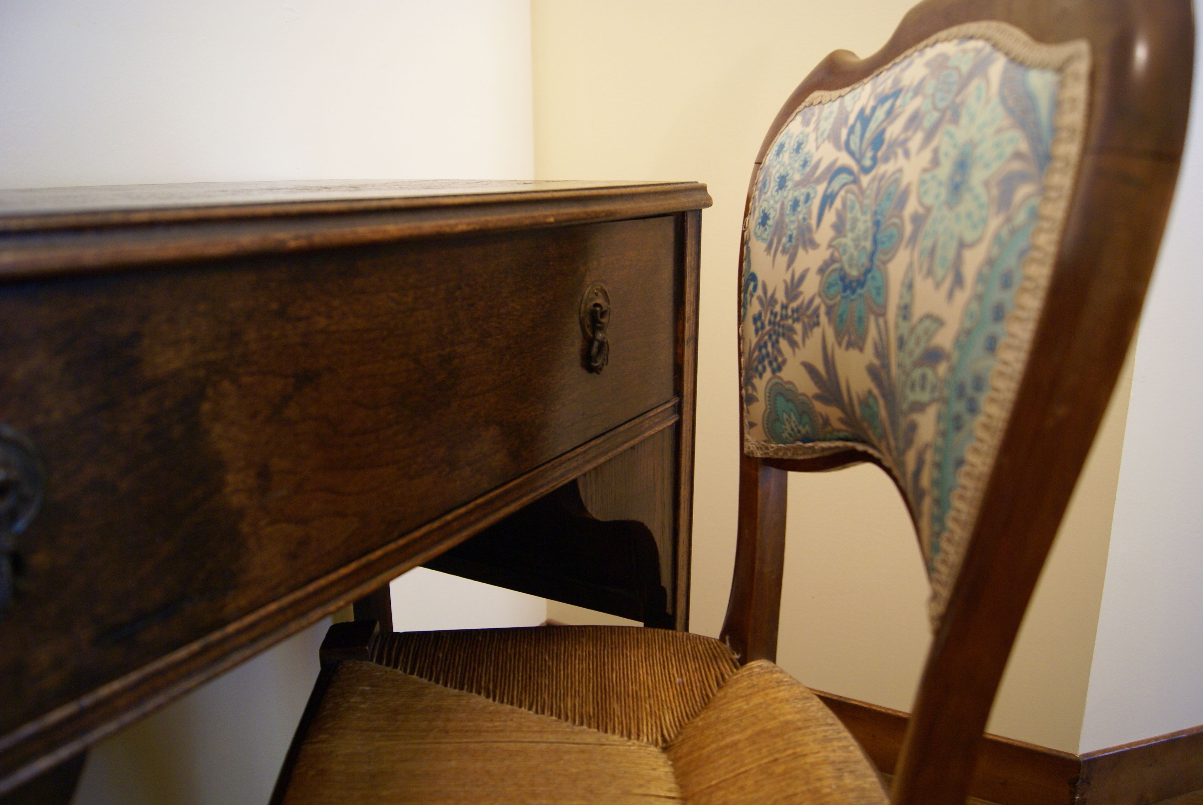 Un aparador de madera con un cajón y una silla con respaldo estampado con motivos florales.