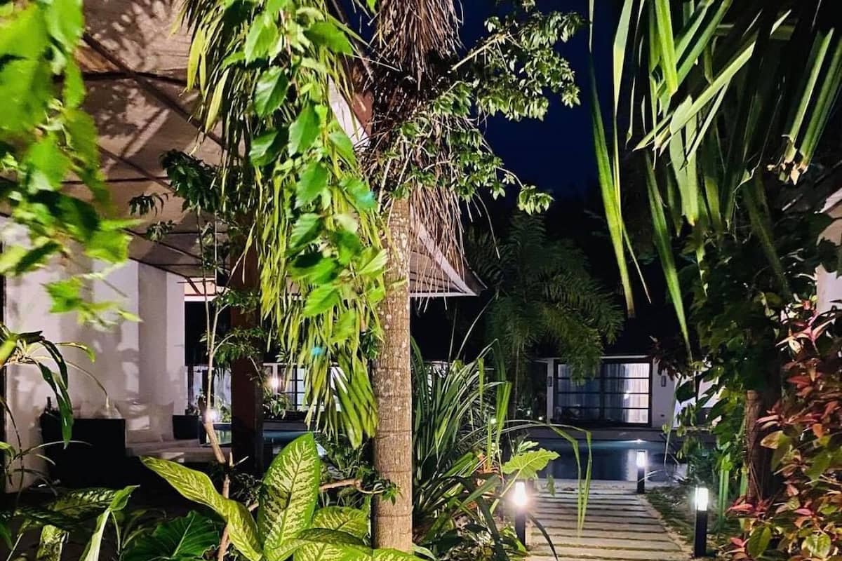 A nighttime garden pathway leading to a building with a thatched roof.