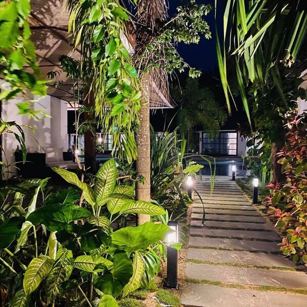 A nighttime garden pathway leading to a building with a thatched roof. - Siargao Bleu Resort And Spa (General Luna)