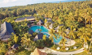 Un resort con piscina central rodeada de palmeras y construcciones de techo de paja.