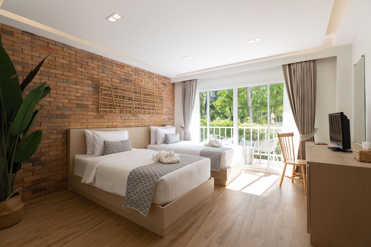 A modern hotel room with a brick accent wall, two beds, a balcony with a view, and a desk with a TV.