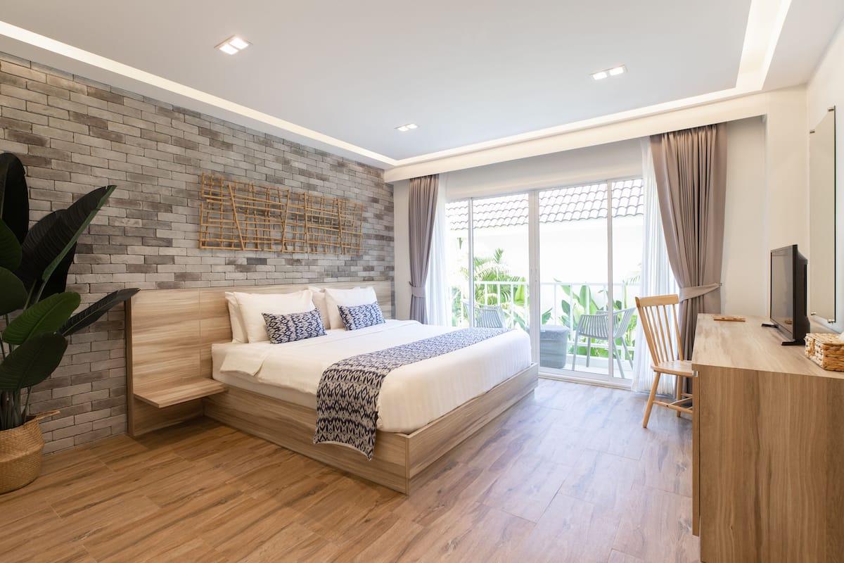 A modern bedroom with a large bed, a brick accent wall, and a balcony with outdoor furniture.