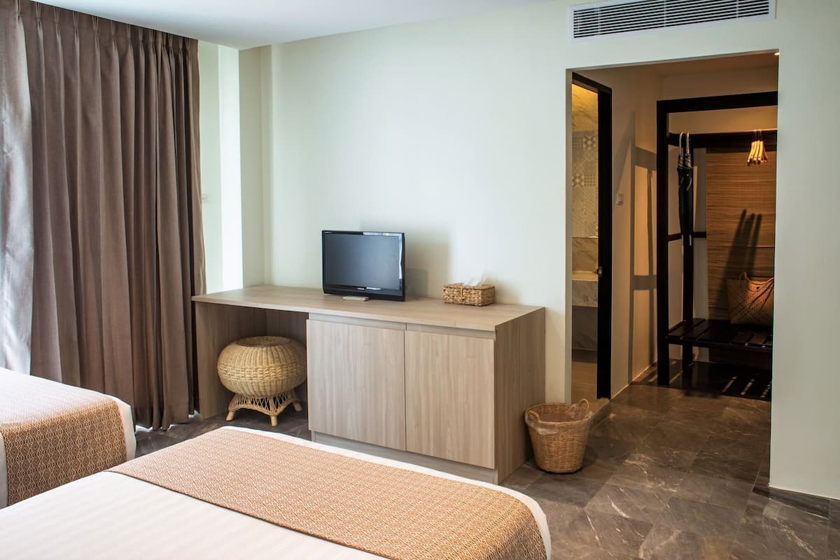 A hotel room with a bed, a desk with a television, a wicker stool, and a bathroom visible through an open door.