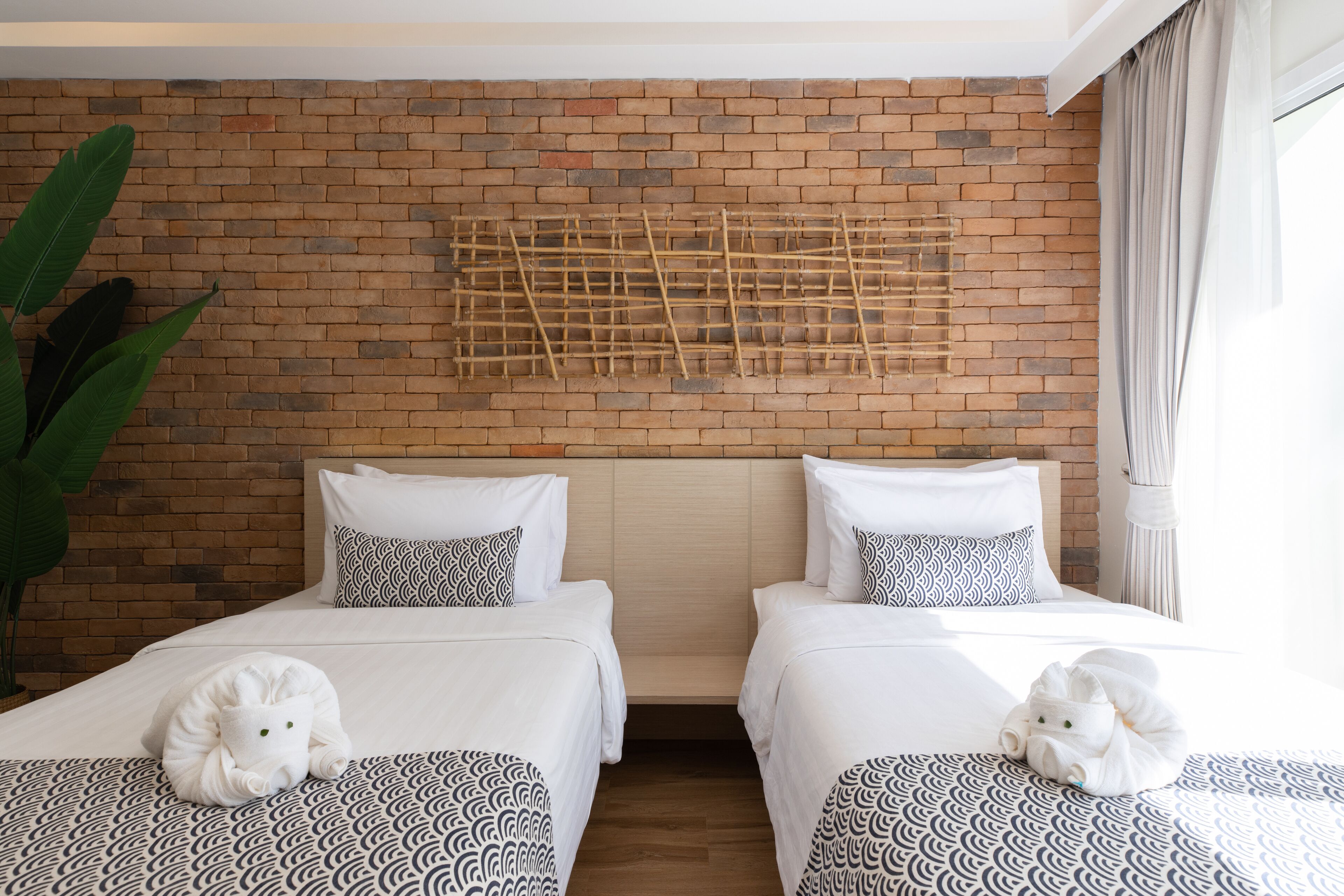 Habitación de hotel con dos camas, una pared de ladrillo y una planta grande.