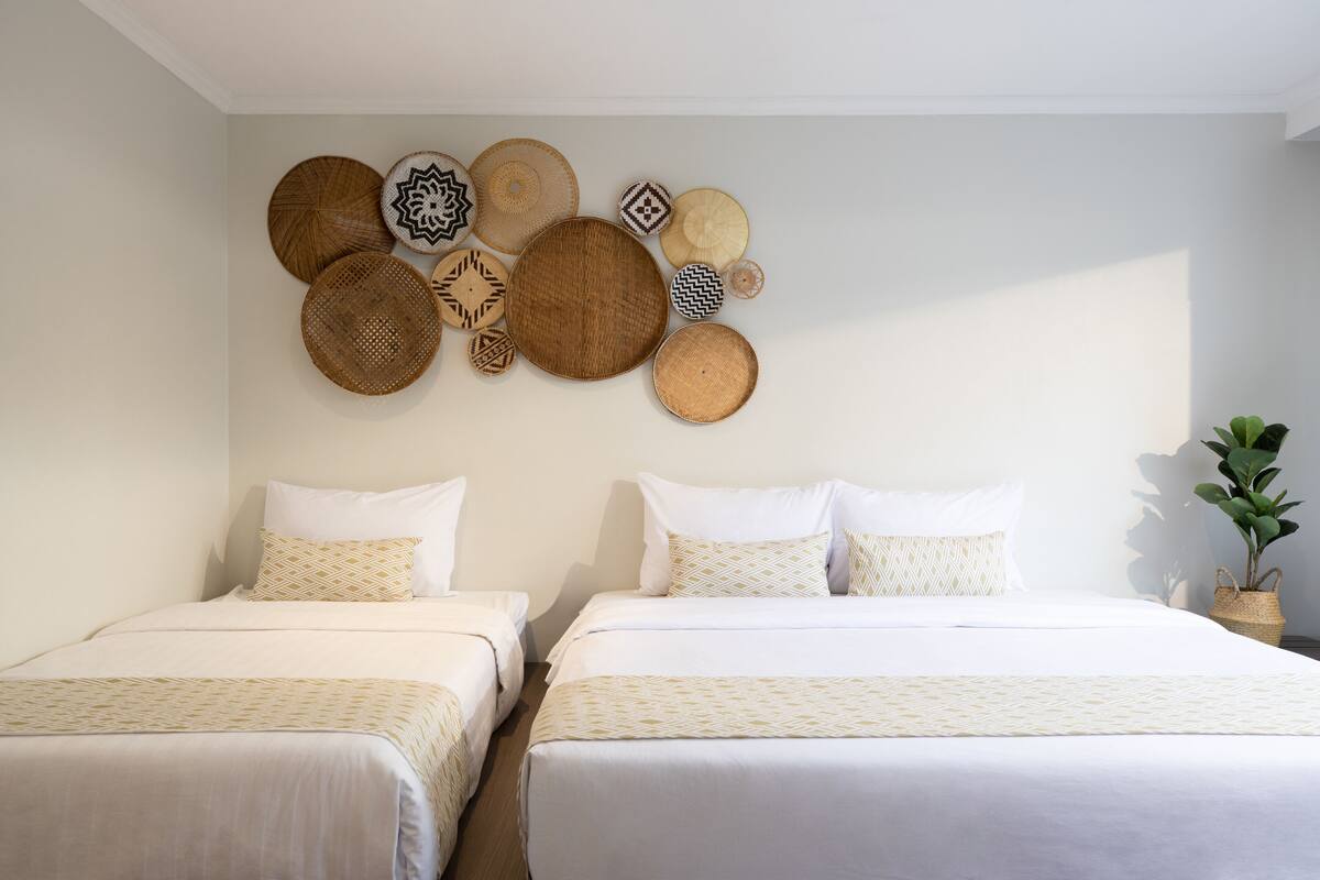 A hotel room with two beds, a wall decorated with woven baskets, and a potted plant.