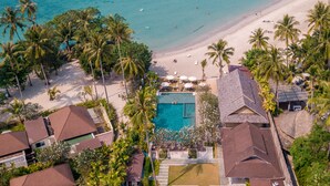 Luchtbeeld van een resort met een centraal gelegen zwembad, een strand en dichte palmbomen.