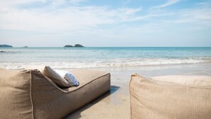 Een strand met twee beige loungestoelen en uitzicht op de oceaan en verre eilanden.