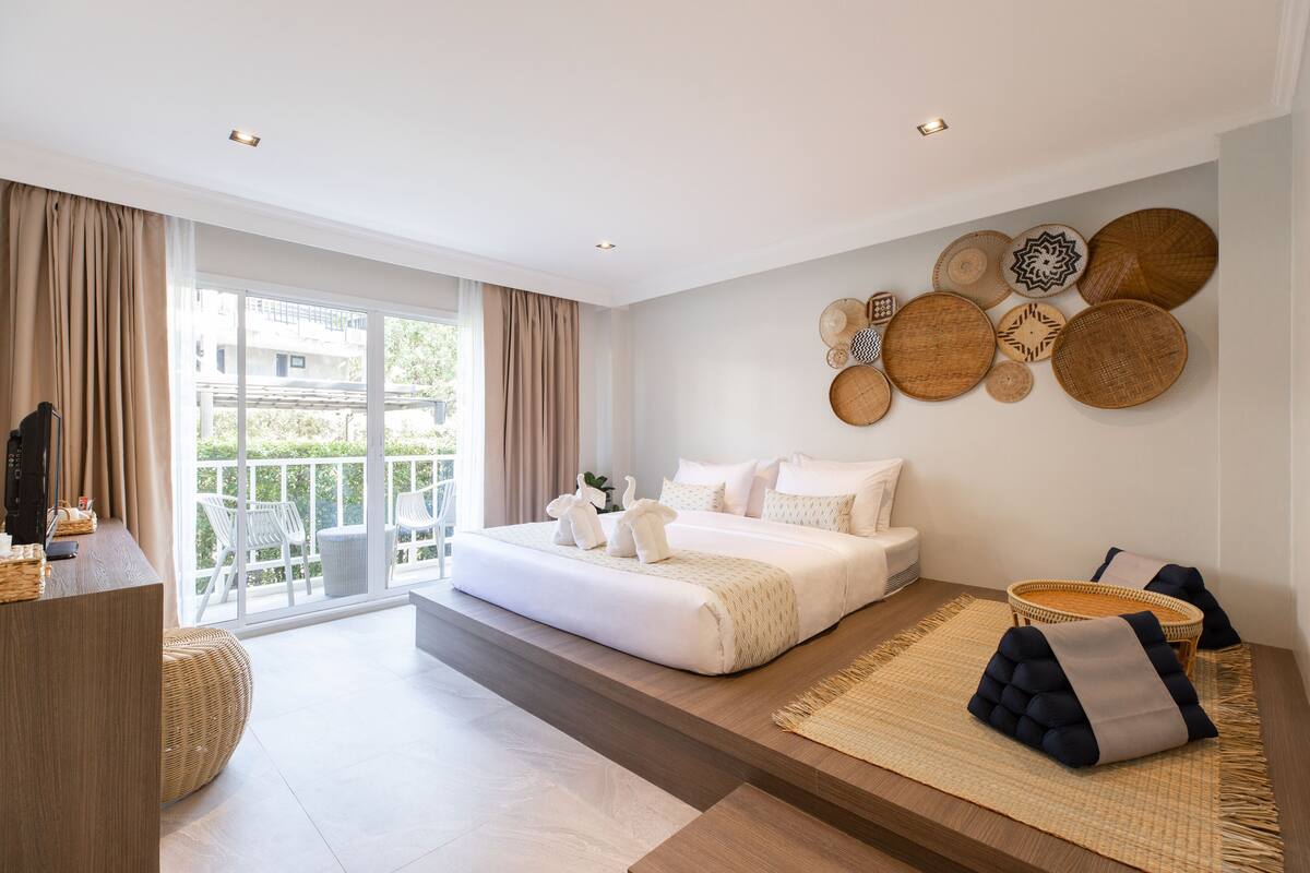 A modern hotel room with a large bed, a balcony with chairs, and a wall decorated with woven plates.