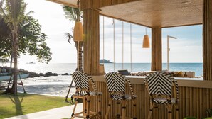 Een houten zitgedeelte buiten met stoelen en een tafel, met uitzicht op een strand en zee.