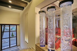 A hotel lobby with a modern design, featuring a staircase, red seating, and large decorative columns with water effects.