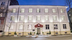 Un edificio grande de varios pisos con fachada simétrica, múltiples ventanas y una entrada central con toldo rojo.