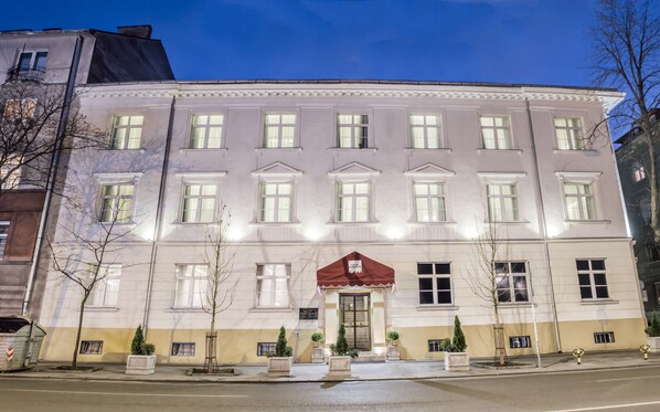 A large, multi-story building with a symmetrical facade, multiple windows, and a central entrance with a red awning.