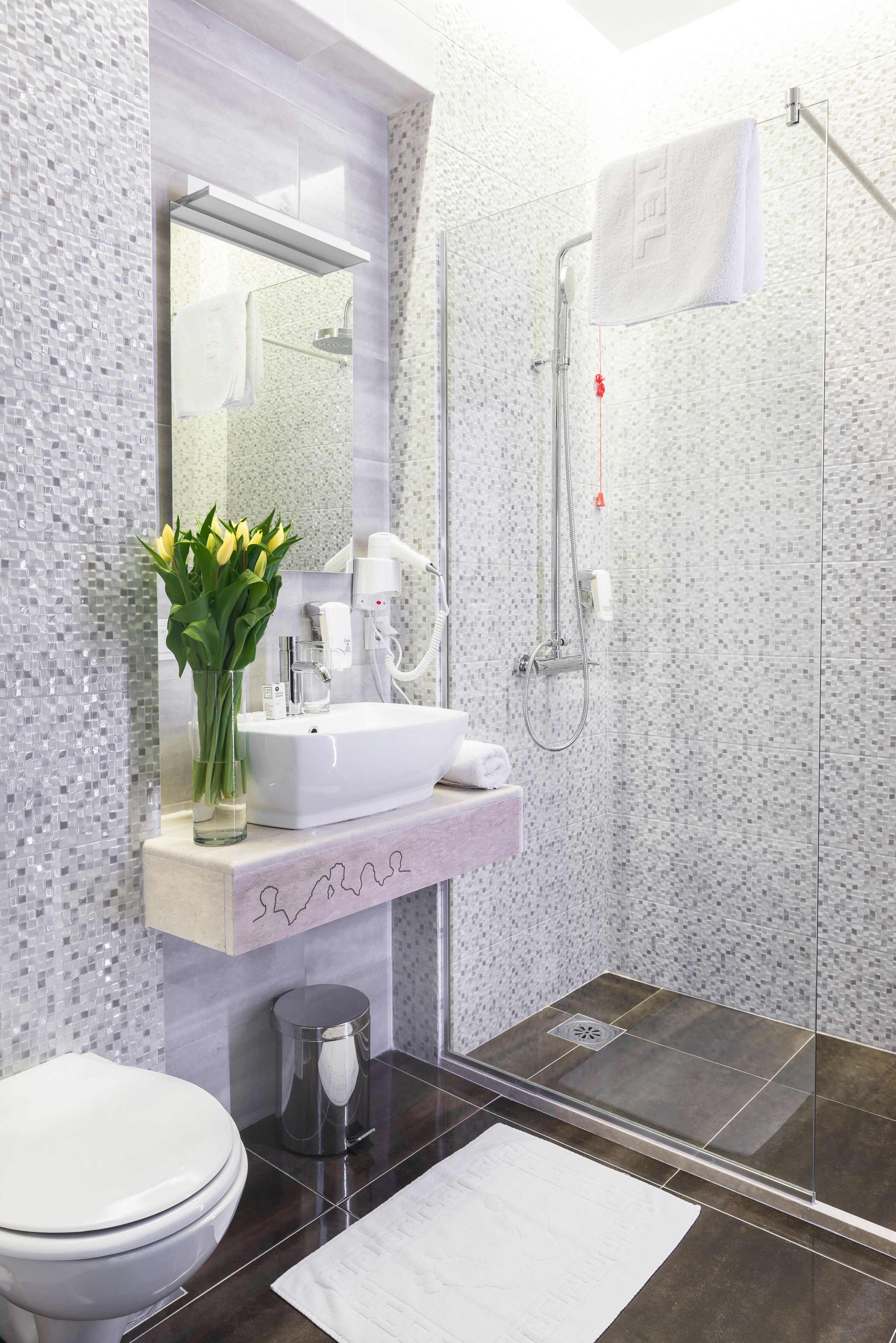 A modern bathroom with a white sink, a glass vase with flowers, a toilet, and a shower area.