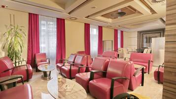 Un hall d’hôtel avec des fauteuils en cuir rouge, une table basse et une grande plante en pot.