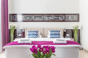A modern hotel room with a large bed, two pillows, a bedside table, a mirror, and a framed picture above the bed.