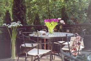 A round outdoor table with chairs, a vase of flowers, and a teapot.