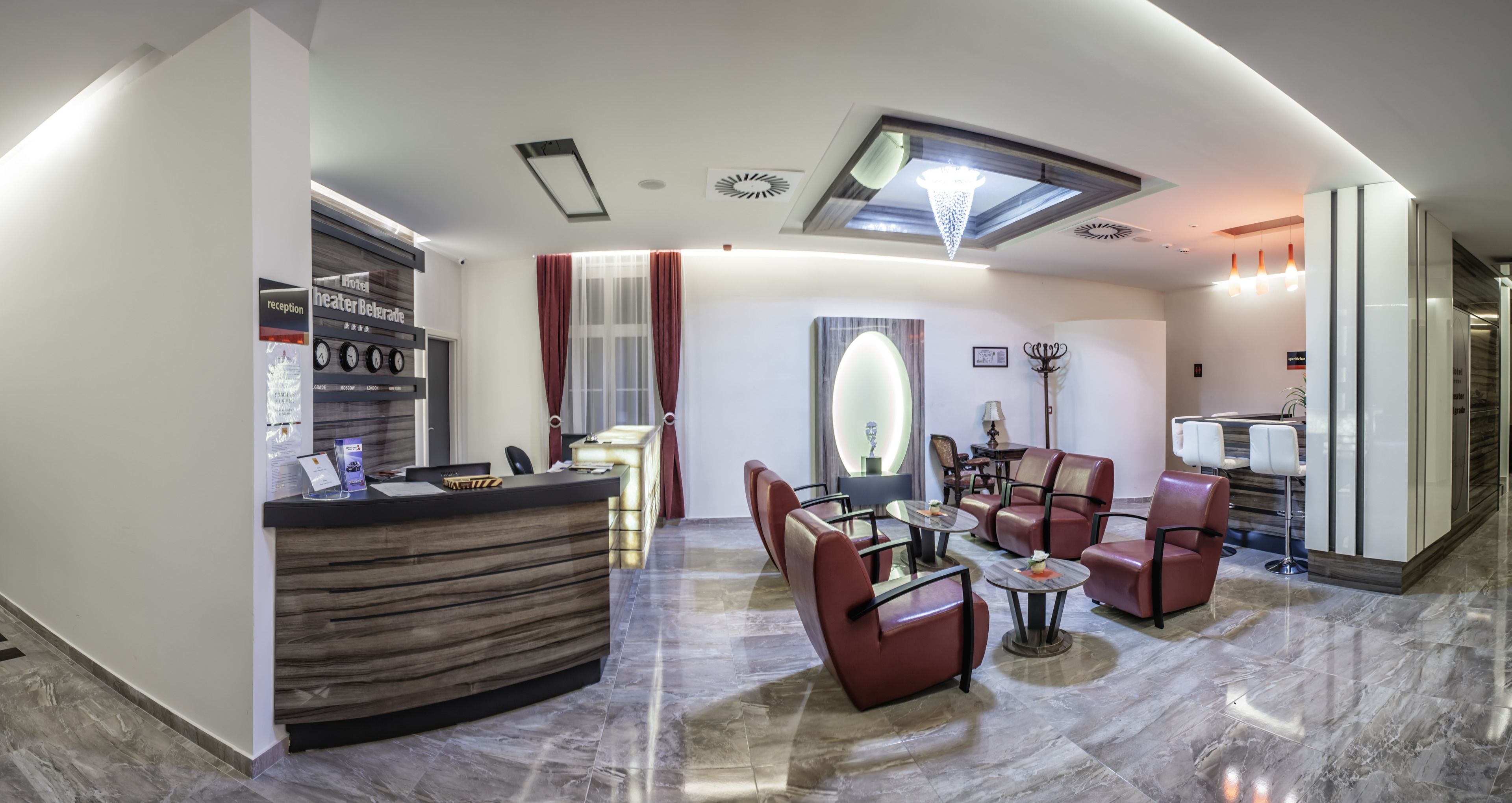 A hotel reception area with a reception desk, seating area with chairs and tables, a chandelier, and a modern interior design.