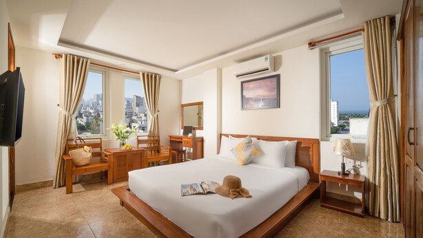 Habitación de hotel con una cama grande, un escritorio con una silla, un televisor y una ventana con cortinas.