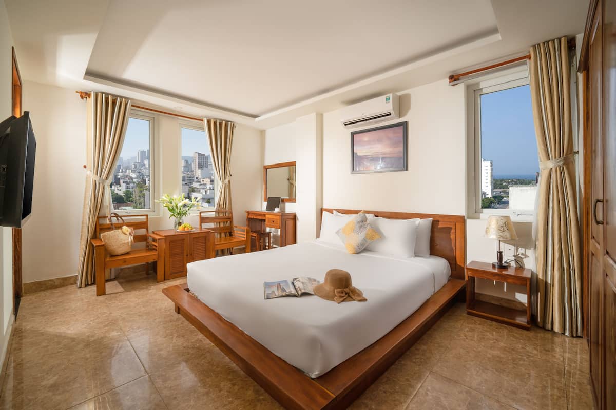 A hotel room with a large bed, a desk with a chair, a TV, and a window with curtains.