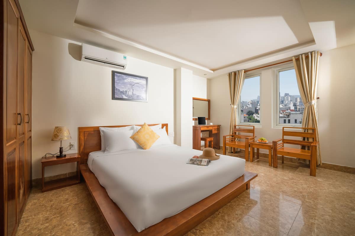A hotel room with a large bed, a desk, a chair, and a view of the city.