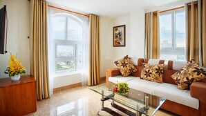 Una sala de estar con sofá, mesa de centro de vidrio, mesita auxiliar de madera y ventana con cortinas.