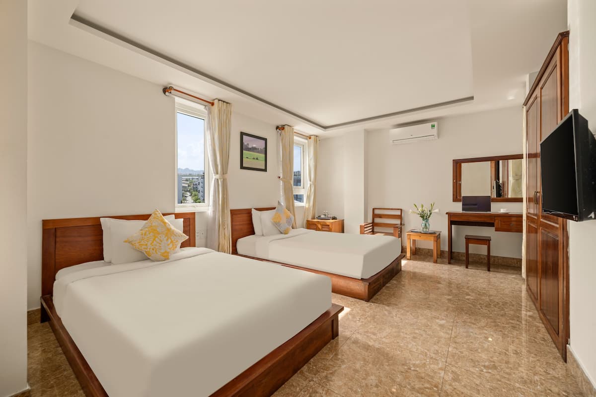 A hotel room with two beds, a desk, a chair, a television, and a window with curtains.