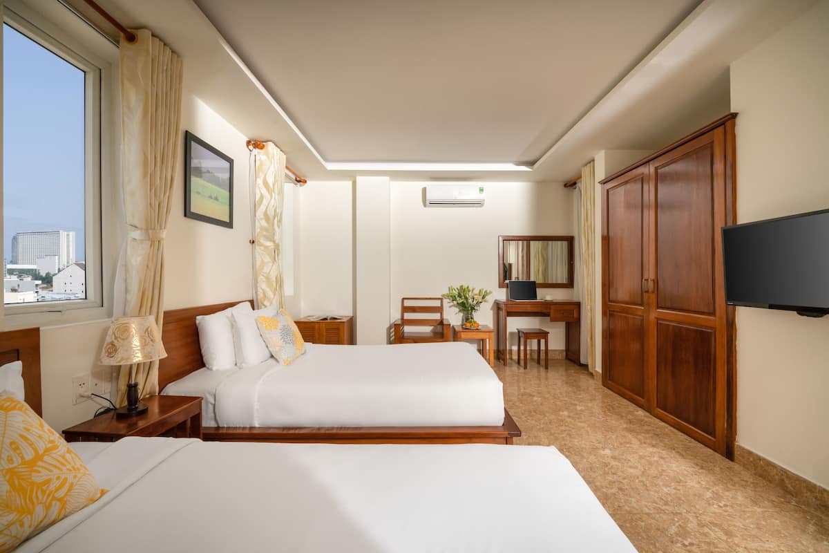 A hotel room with two beds, a desk, a chair, a TV, and a window with curtains.