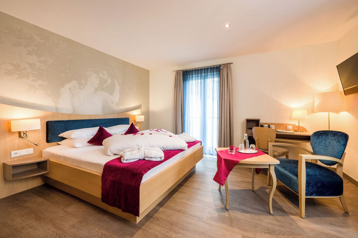 A hotel room with a bed, bedside tables, a desk, a chair, and a window with curtains.
