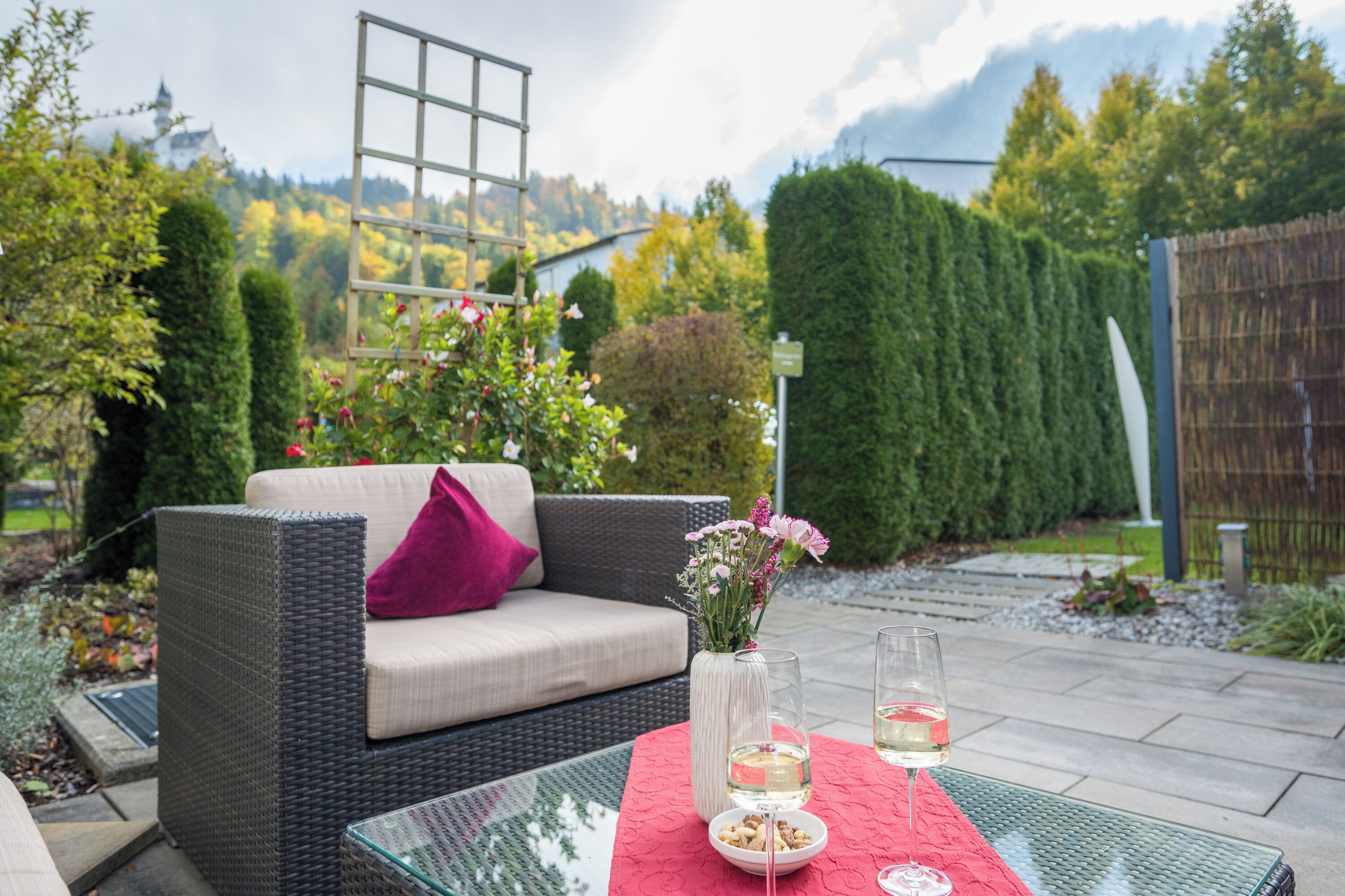 A wicker sofa with a cushion and a vase of flowers on a glass table with a red tablecloth.