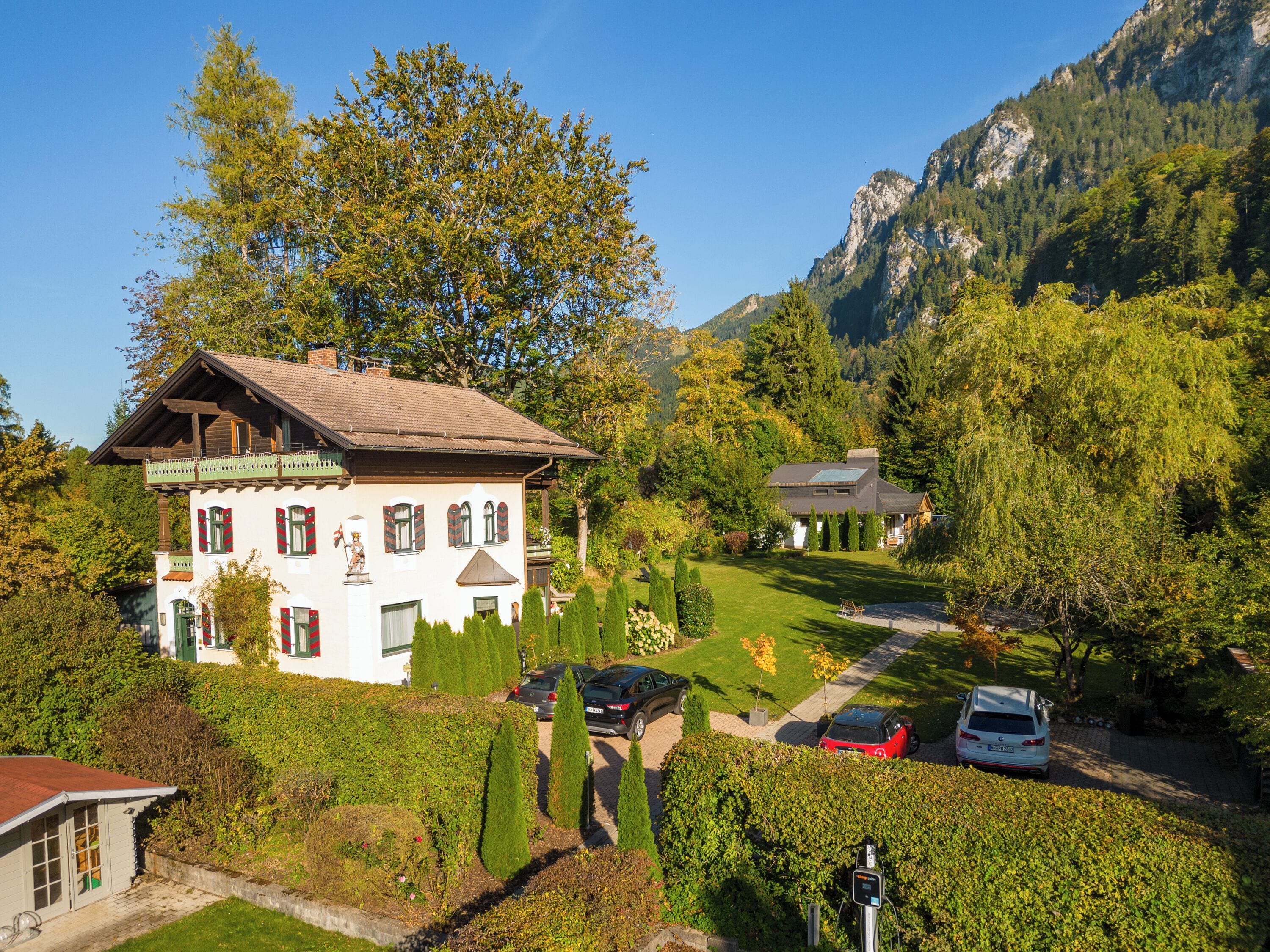 A traditional chalet-style building with a sloped roof, surrounded by lush greenery and a mountainous backdrop.
