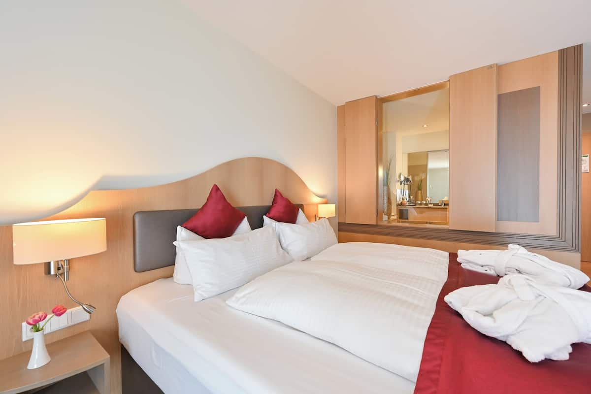 A hotel room with a large bed, a nightstand with a lamp, a mirror, and a red bedspread.