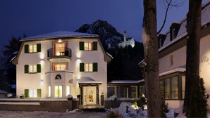 Hotel Villa Ludwig Suite, de dos pisos, con fachada nevada, un balcón en el segundo piso y una entrada bien iluminada.