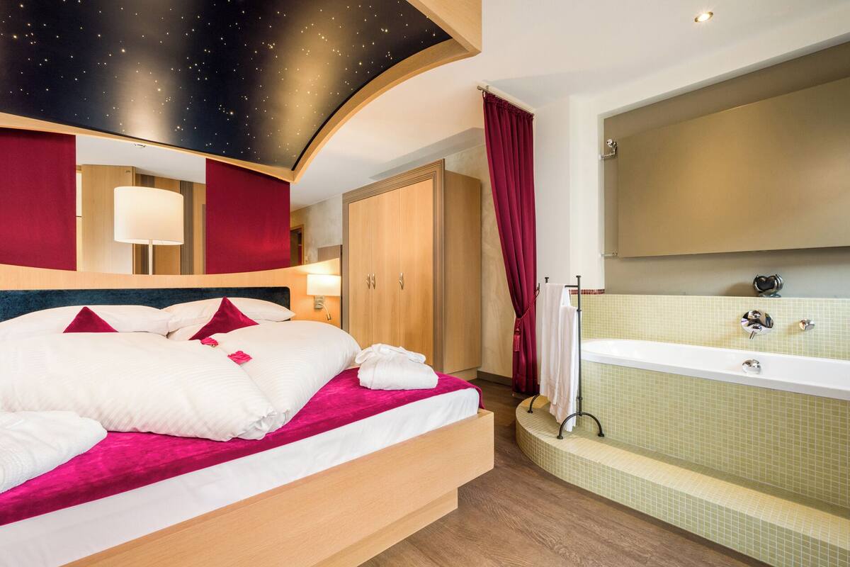 A hotel room with a bed, a large mirror, a bathtub, and a ceiling with a starry design.