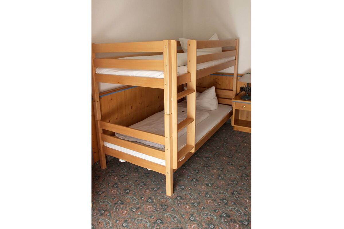 A bunk bed with three levels, a bedside table, and a patterned carpet.