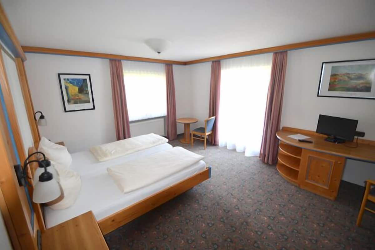 A hotel room with a single bed, a desk with a computer, a chair, and a small table.