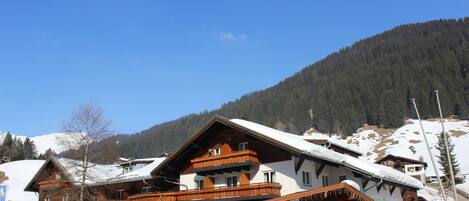 Un edificio de madera de varios pisos, con balcones, rodeado de árboles cubiertos de nieve y una montaña al fondo.
