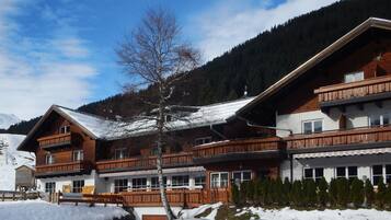 A chalet-style hotel with multiple balconies, wooden exterior, and a mountain backdrop.