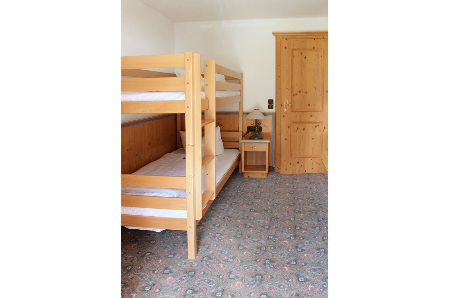 A bunk bed room with a wooden wardrobe and a small bedside table.