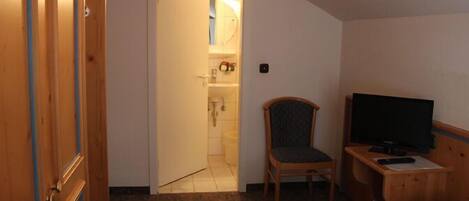 A hotel room with a bed, a TV, a chair, and a bathroom visible through an open door.