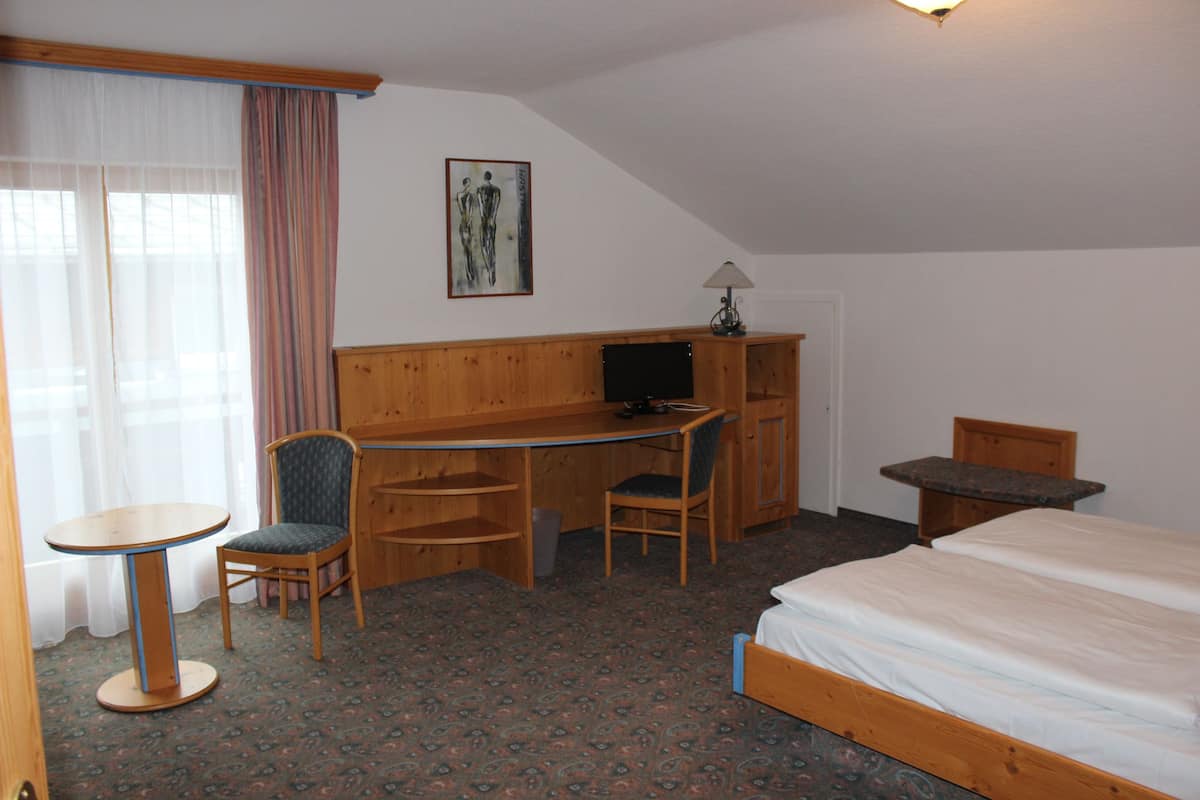 A hotel room with a bed, a desk with a chair, a small table, and a television.