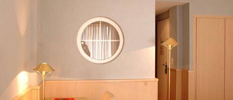 A room with a round window, a desk with a lamp, a chair, and a wardrobe.