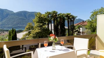 Un balcon avec une table dressée pour deux personnes, offrant une vue sur un paysage montagneux et un plan d’eau.