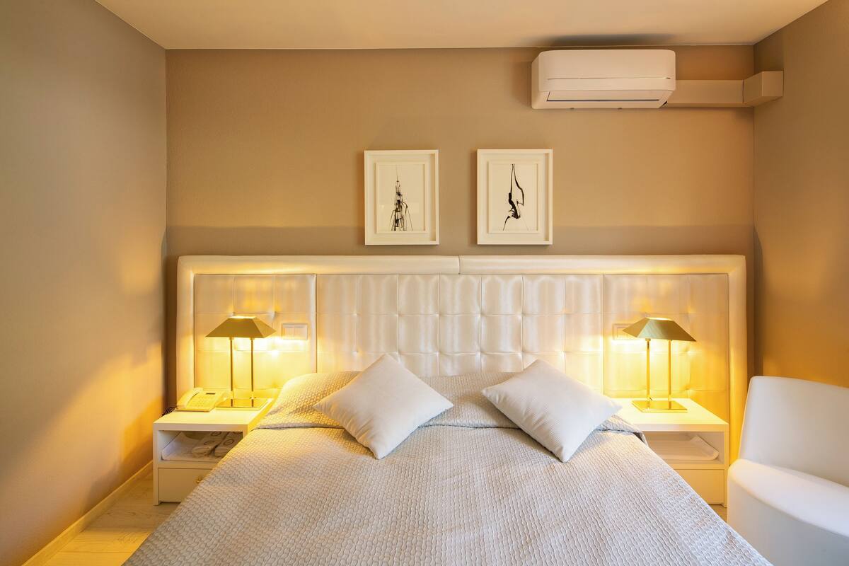 Un dormitorio ordenado con una cama grande, dos mesitas de noche con lámparas, un cabecero y dos cuadros enmarcados en la pared.