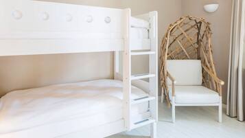 Uma cama beliche com cabeceira branca e uma cadeira branca com encosto de fibra trançada.