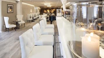 A modern hotel lobby with white leather seating, a bar area with a large candle, and a decorative wall with vertical panels.