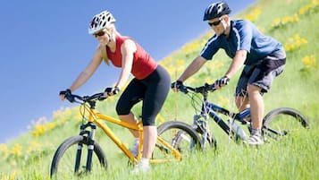 Two cyclists on a grassy hill with a clear sky.