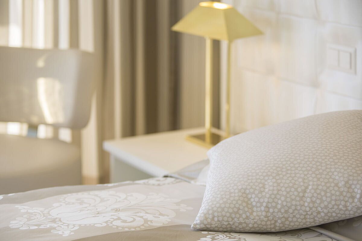 Un lit bien fait, recouvert d’une couvre-lit à motifs et agrémenté d’un oreiller blanc à pois.