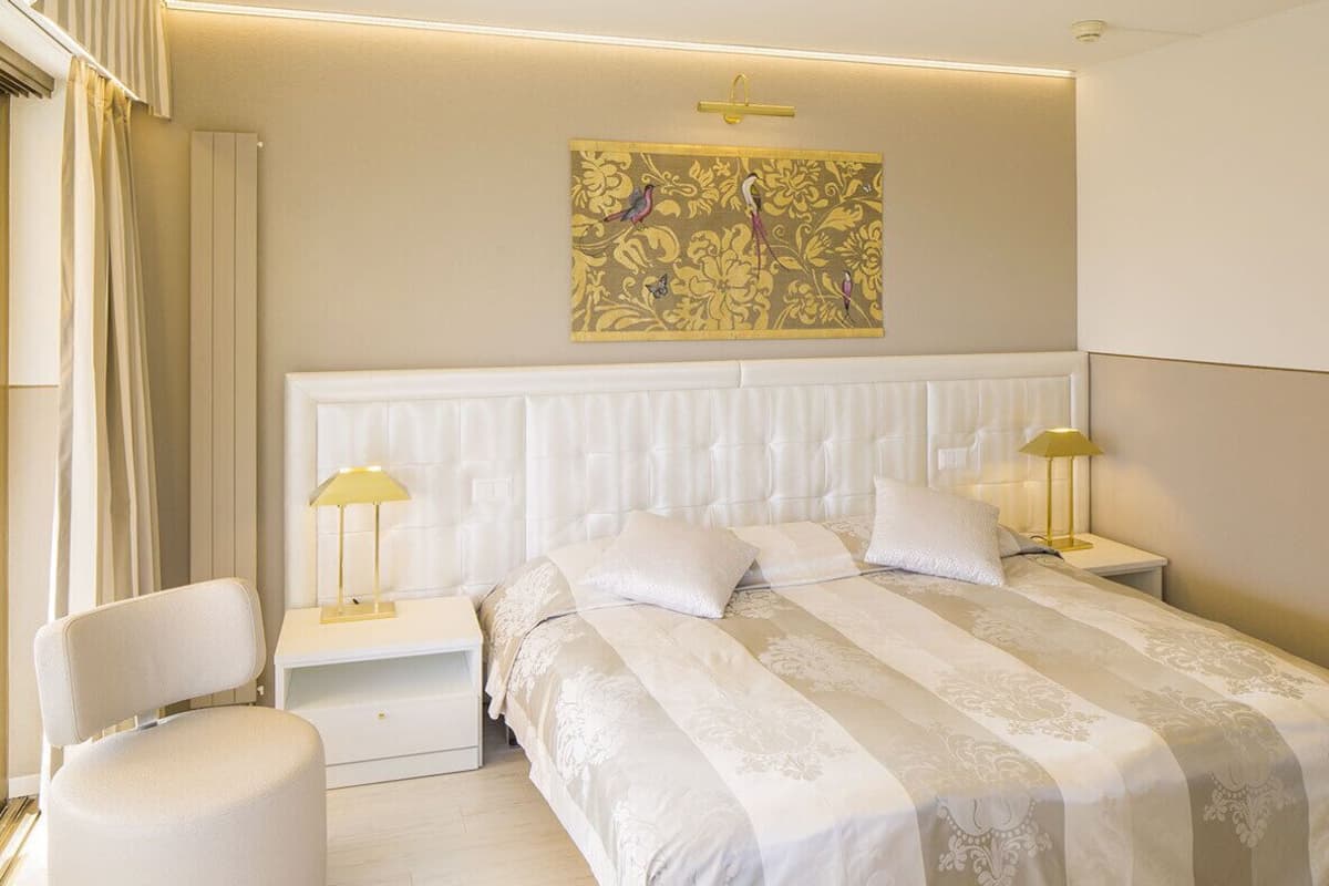 Un dormitorio moderno con una cama grande, dos mesitas de noche con lámparas, una silla y un adorno en la pared.
