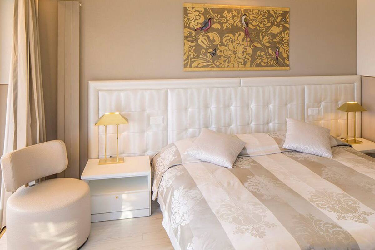 Habitación de hotel con una cama grande, dos mesitas de noche, una silla y un adorno de pared.
